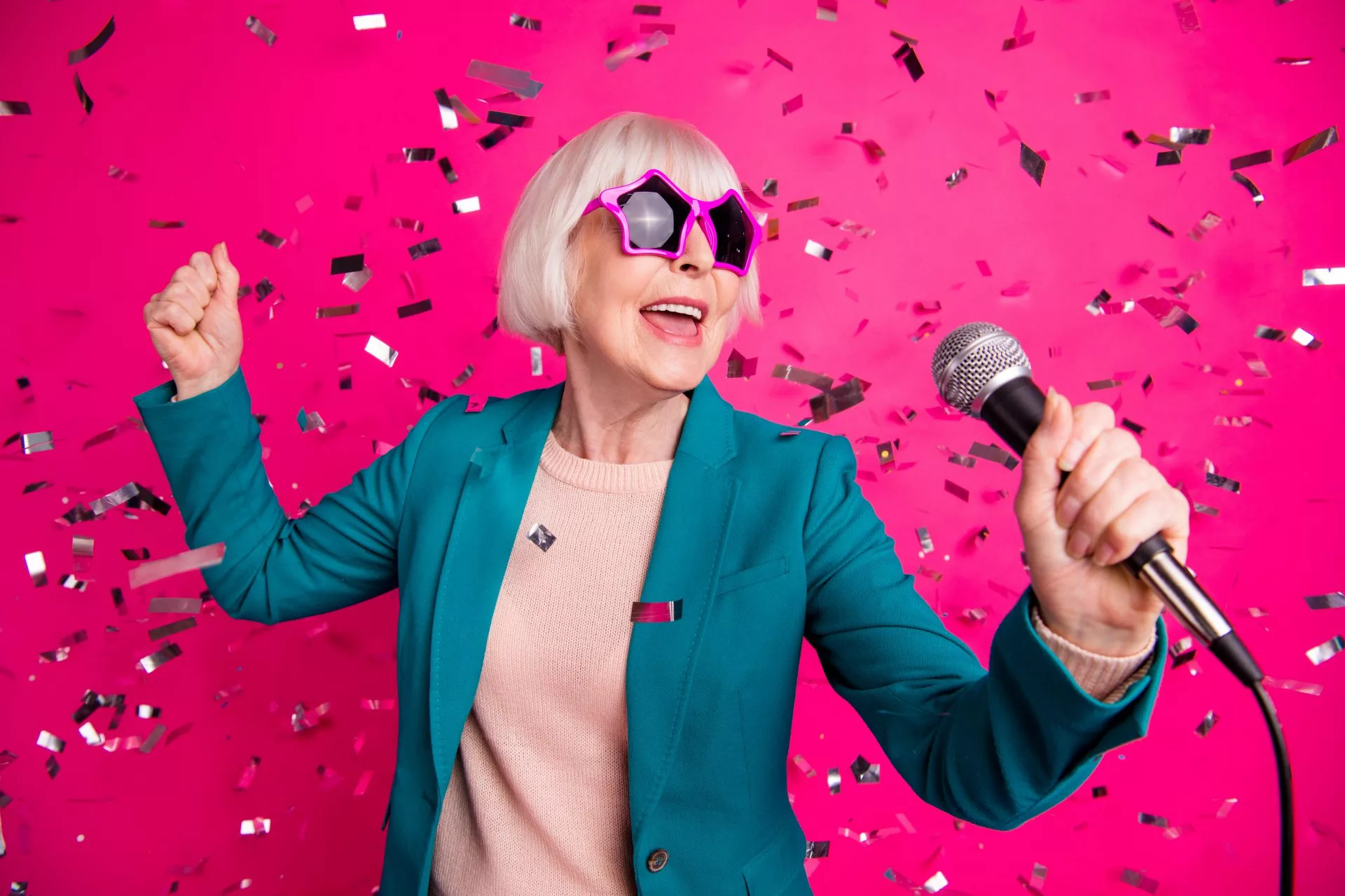 Senior lady singing in to a microphone wearing start shaped glasses