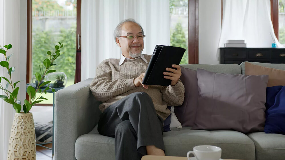 Senior man appears to be enjoying himself while holding a tablet, possibly learning from one of Inclusee's learning interest programs.