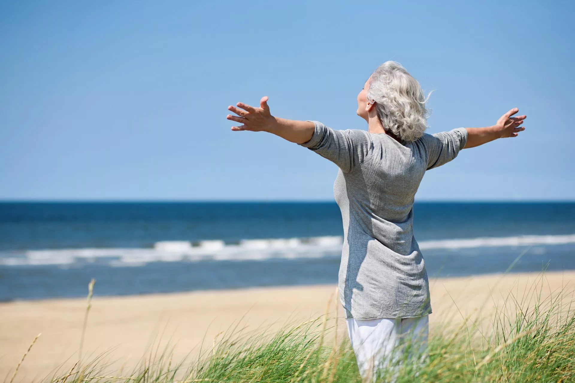 Senior woman embracing the wind, feeling wellness by the shore.
