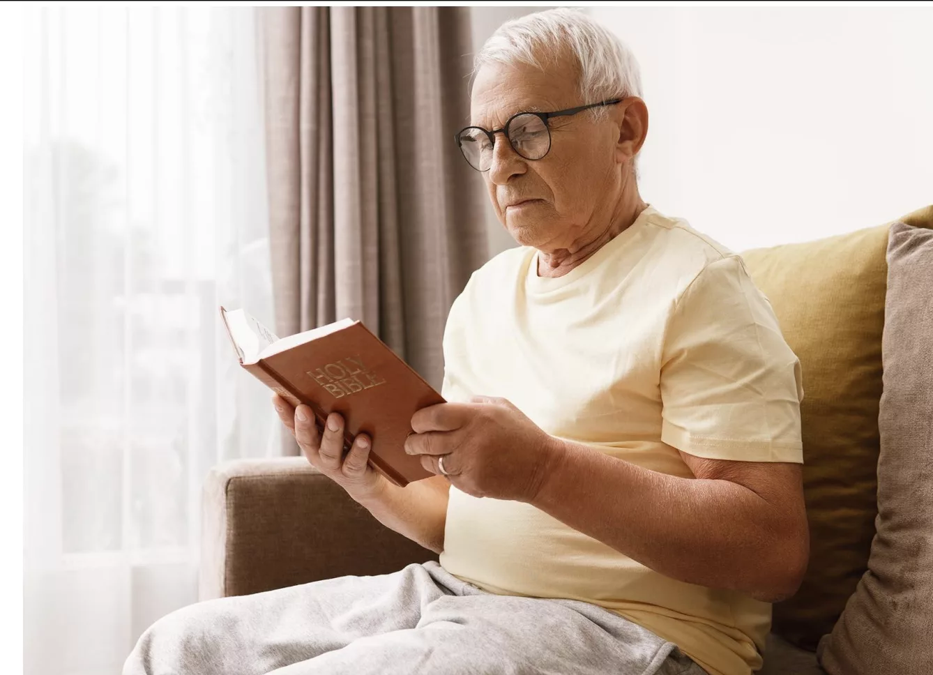 Elderly man reading Bible at home.