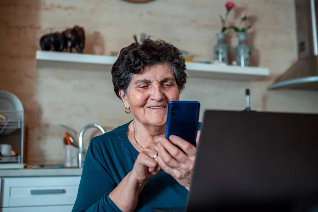 Elderly woman using phone, likely connecting with family online.