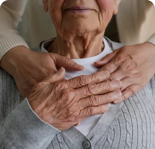 Close-up of an elderly person with another person's hands gently resting on their shoulders.